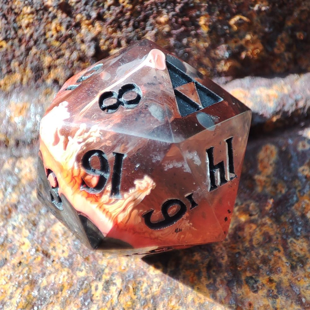 A close up of a fiery red/orange d20 with the Triforce logo in place of a 20. You can see defined drips of white and orange ink on the inside.