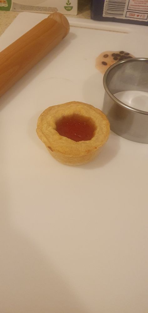 a small jam tart on a cutting board, with a rolling pin and cookie cutter beside it