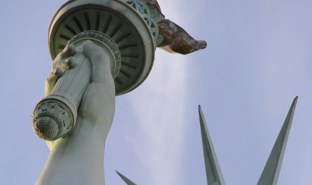 The arm of the Statue of Liberty holding up its torch towards a blue sky.