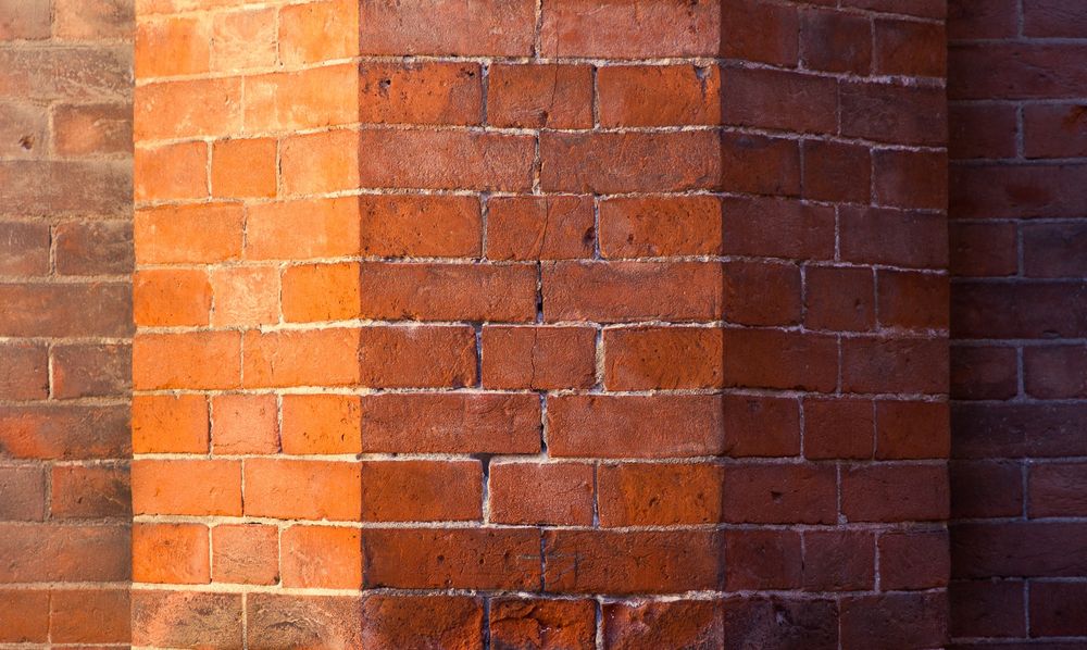 Straight-on photo of a brick wall with a polygonal protrusion catching warm light on the left of the frame, shadowed and blue to the right. The effect is of 5 vertical bands of tone
