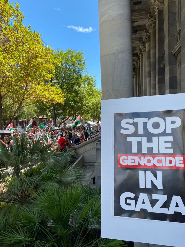 Rally for Palestine outside parliament house. Poster in foreground says stop the genocide in Gaza