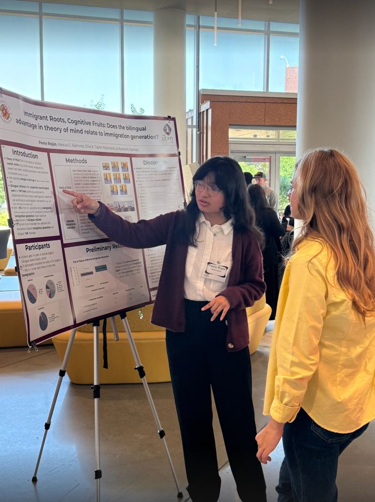 Photo of Paola presenting her poster "Immigrant Roots, Cognitive Fruits: Does the bilingual advantage in theory of mind relate to immigration generation?" to a session attendee