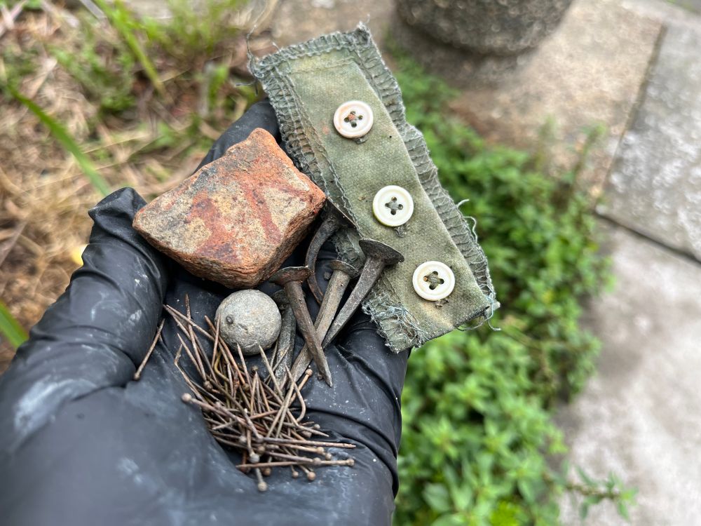 A handful of recent Thames mudlarking finds - from the top; some haberdashery with three buttons, copper nails from barge building, handmade brass dress pins, a musket ball, part of a medieval floor tile. 