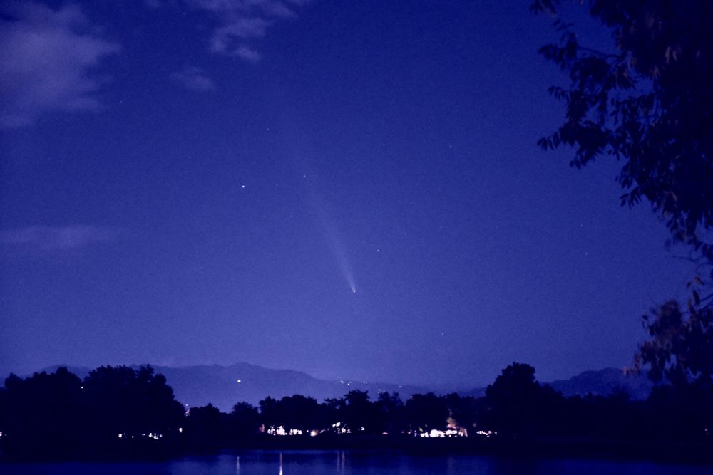 A long exposure photo of comet tsuchinshan-atlas over the foothills in Colorado with a lake in the foreground