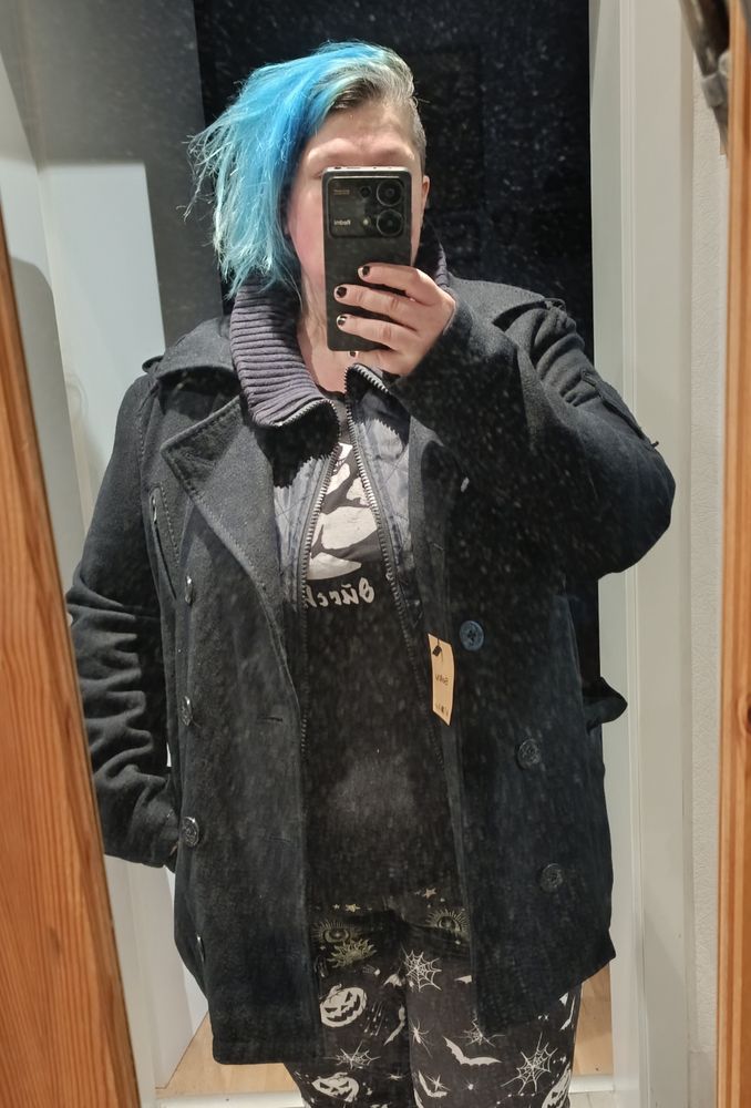 Ich vorm Spiegel in einen hellen Flur, Handy vorm Gesicht und im Fokus steht eine dunkelblaue Cabanjacke. Die Jacke ist offen getragen.