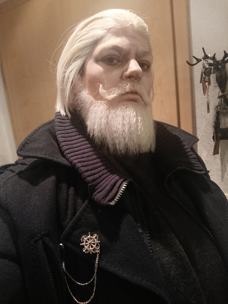 Selfie von mir im Cosplay.
Ich habe eine weiß-blonde Perücke und passenden weiß-blonden Vollbart dazu angeklebt. Ich gucke direkt in die Kamera 