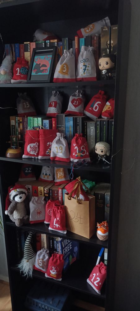 Foto von einem schwarzen Bücherregal, in den ein Adventskalender, bestehend aus selbst gefüllten Stoffsäckchen steht. Dazwischen ein paar Figuren.