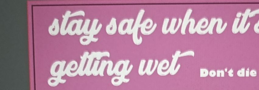 Ausschnitt eines abfotografierten Monitors. Der Hintergrund ist rosa, davor steht in weißer, schnörkeliger Schrift "stay safe when it's getting wet"