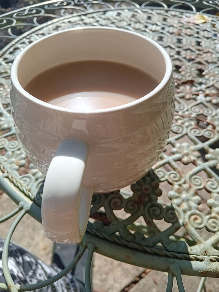 Large mug of tea on wrought iron bistro style table. In the sunshine.