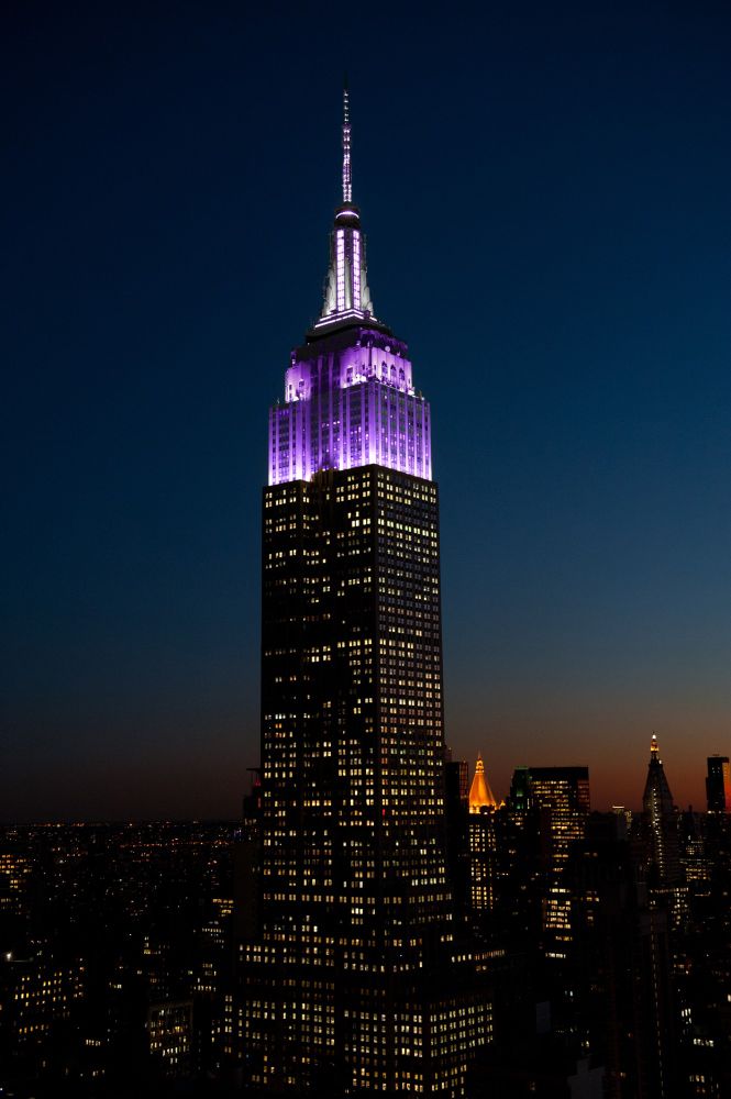Photo of Empire State Building lit in violet against the night sky 