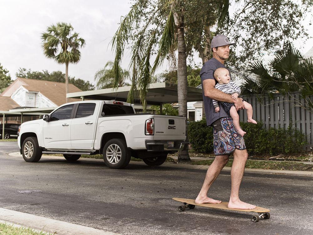 A father carrying his baby while on a skateboard