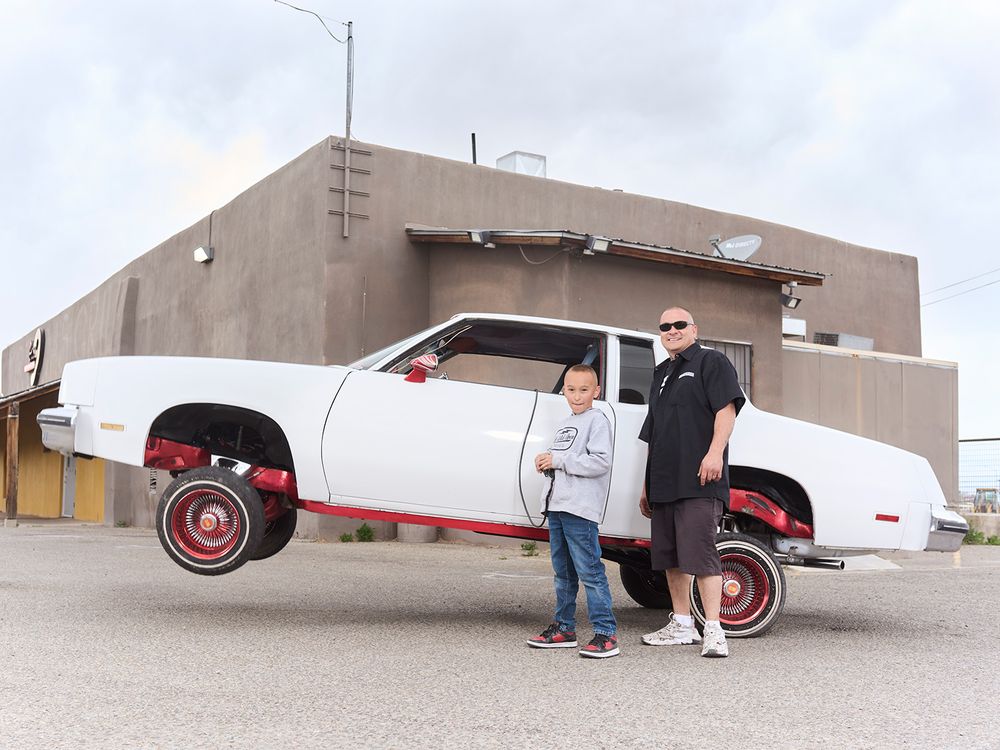 A father and son standing in front of a lifted car
