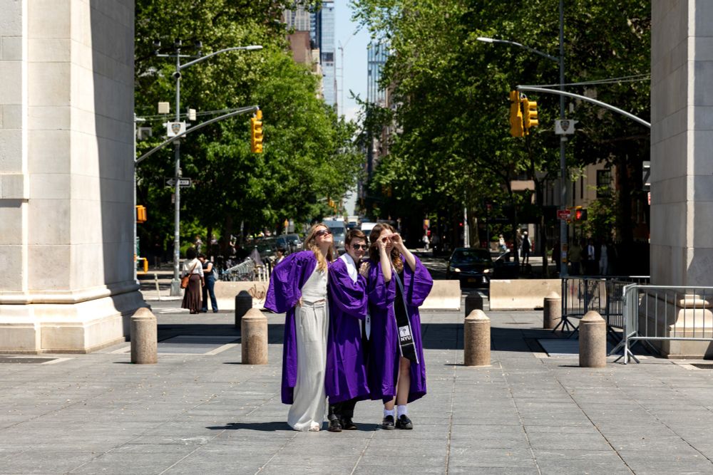 three NYU grads in purple robes posing with sunglasses under the arch in Washington Square Park