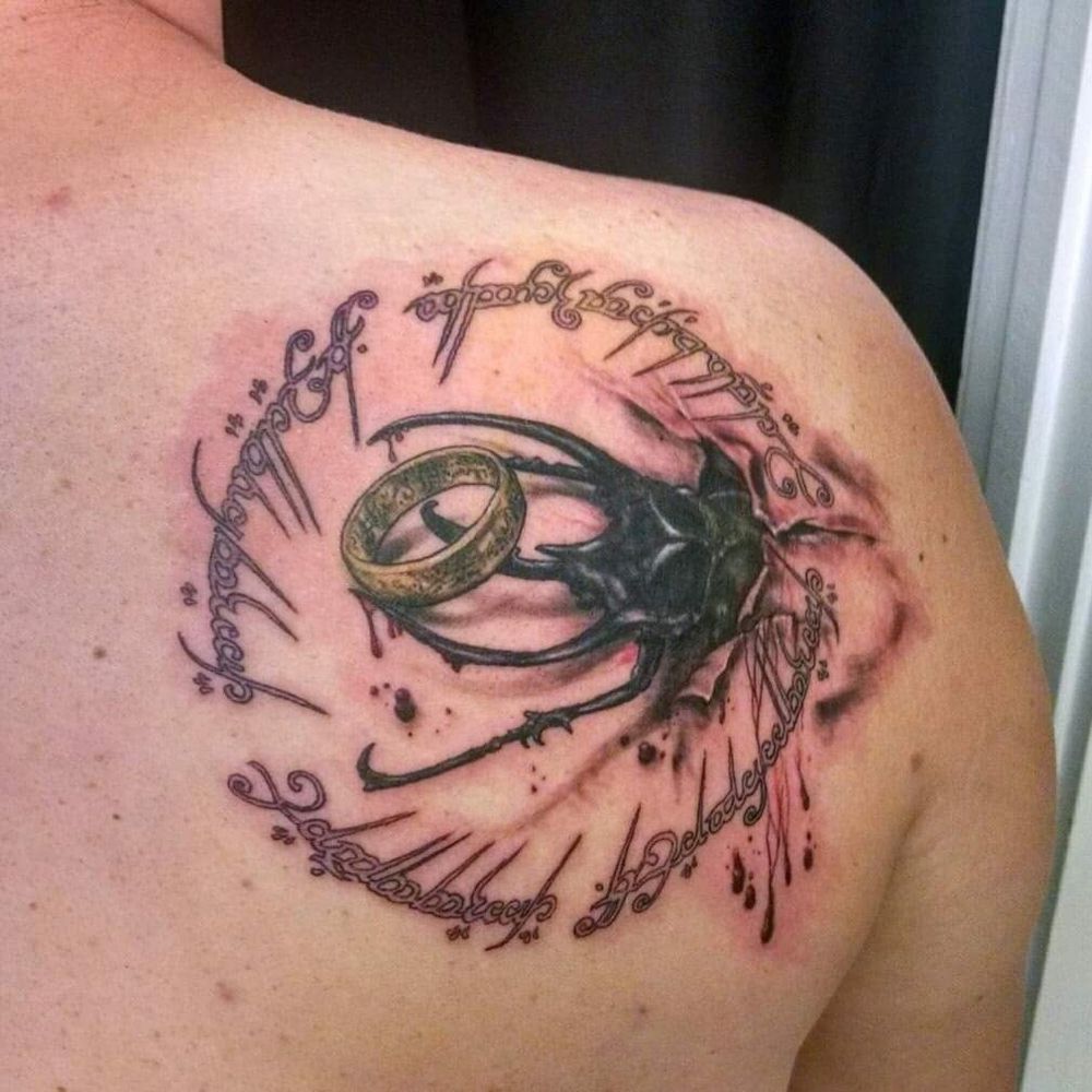 Image of a tattoo with a large beetle burying out of human skin with the One Ring from Lord of the Rings on its horn surrounded by the One Ring poem in elfish script.