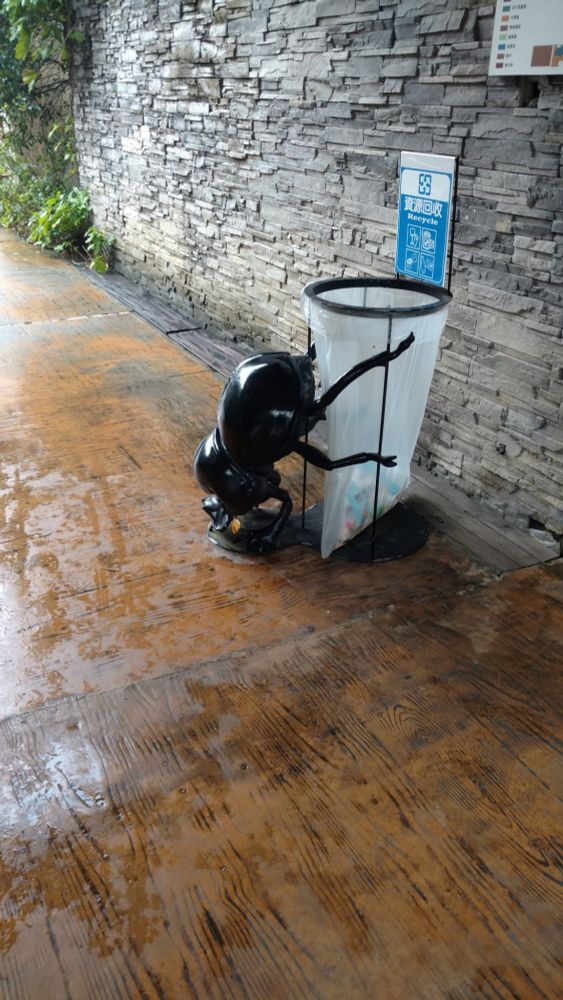 Enlarged dung beetle figure trying to roll a garbage can.