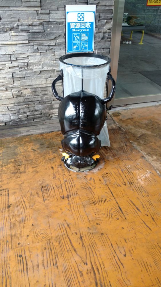 Enlarged dung beetle figure trying to roll a garbage can.