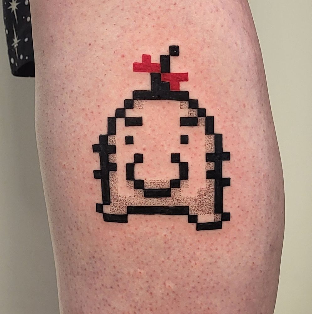 A close up shot of the side of my calf with a fresh tattoo of Mr Saturn from Earthbound with its pixels sized way up.