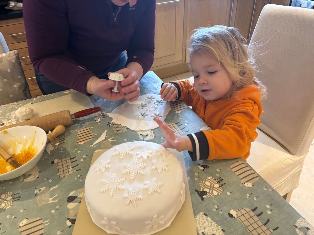 Mackenzie - a little girl in an orange hoodie - and Kirstie (but with her head cut off!) are adding icing snowflakes to the Christmas cake