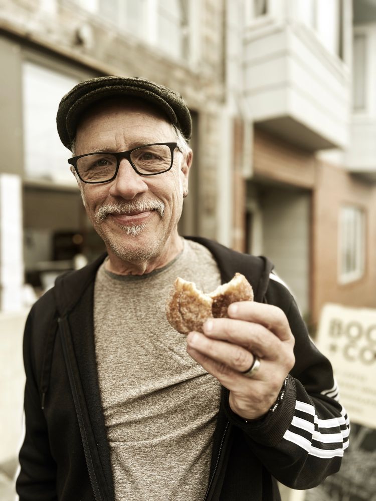John Seckman holding an apple-cinnamon donut with a bite taken out of it. 