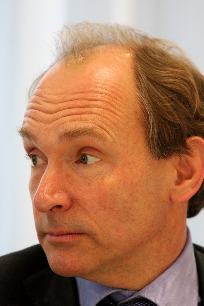 Photo de Tim Berners-Lee, vêtu d’une chemise blanche et d’une cravate noire. Ses cheveux gris sont légèrement clairsemés sur le dessus. L’arrière-plan est blanc, mettant en évidence la personne au premier plan.