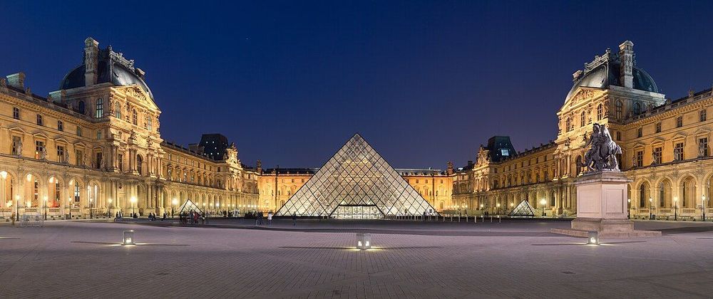 La cour Napoléon du musée du Louvre à Paris la nuit, avec la pyramide du Louvre illuminée au centre, entourée par les ailes du palais du Louvre.