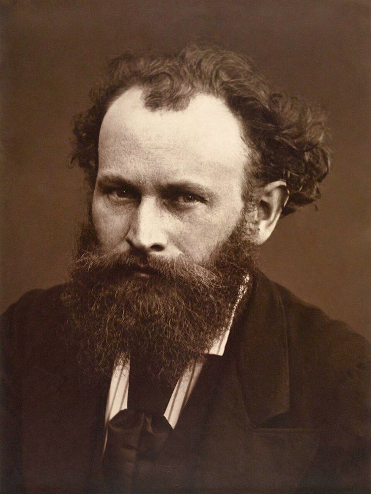 Photo en buste en noir et blanc d'Édouard Manet, de face. Il a un regard intense, de longs cheveux qui tombent sur les oreilles et une barbe épaisse. Il porte une veste sombre sur une chemise claire.