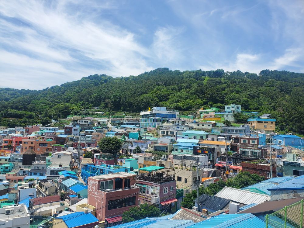 A wide vista looking out over brightly colored houses that extend up the side of a mountain in terraces. This is Gamcheon Culture Village in Busan.