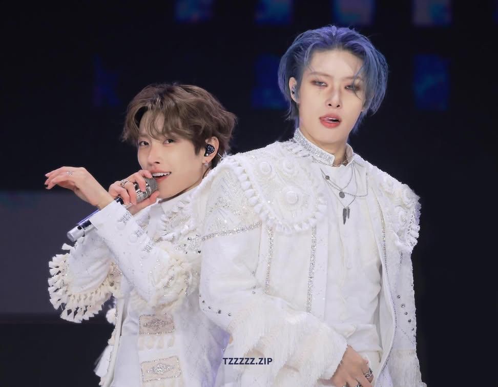 Mingi standing on stage with Hongjoong slightly behind him, both in all-white stage outfits.