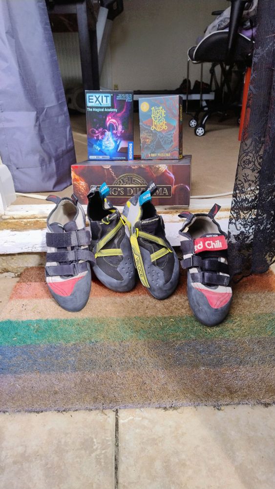 Picture of two old battered pairs of climbing shoes, some board games and a ragged old pride flag doormat