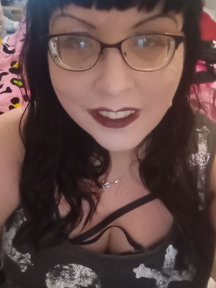 Selfie of Isabelle. She's wearing glasses, a black tank top with white crosses and skulls. 