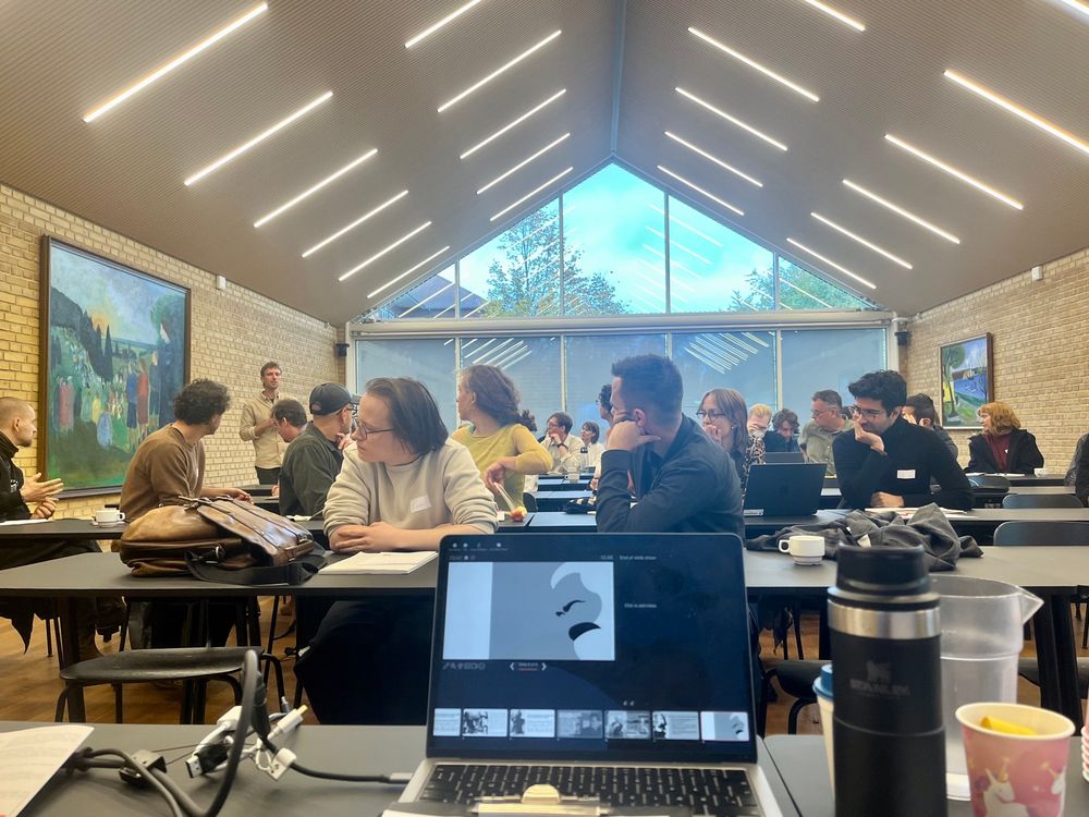 People in a seminar room looking at a person posing a question. In front is a computer screen showing a powerpoint presentation with an image of Marx.