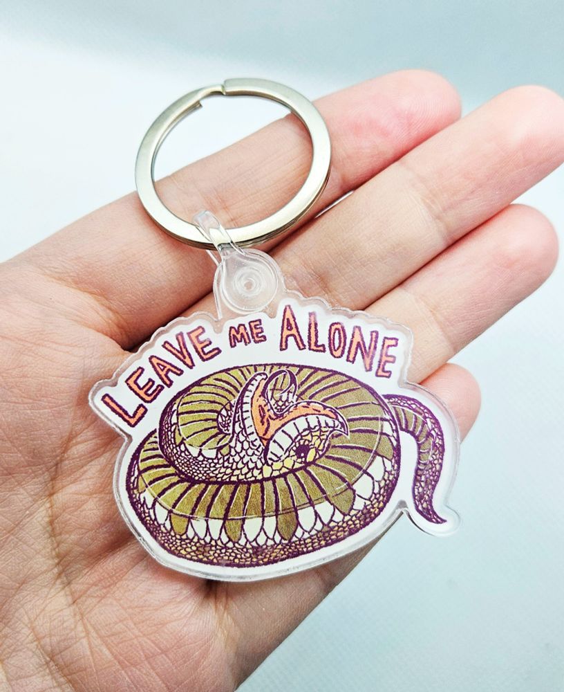 A keychain of a western hognose snake playing dead with the words "LEAVE ME ALONE"