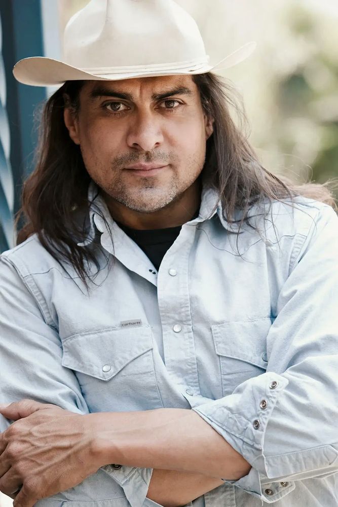 This is a photo of actor Jonathan Joss. He has his arms folder that he's looking straight at the camera and he looks very handsome. 