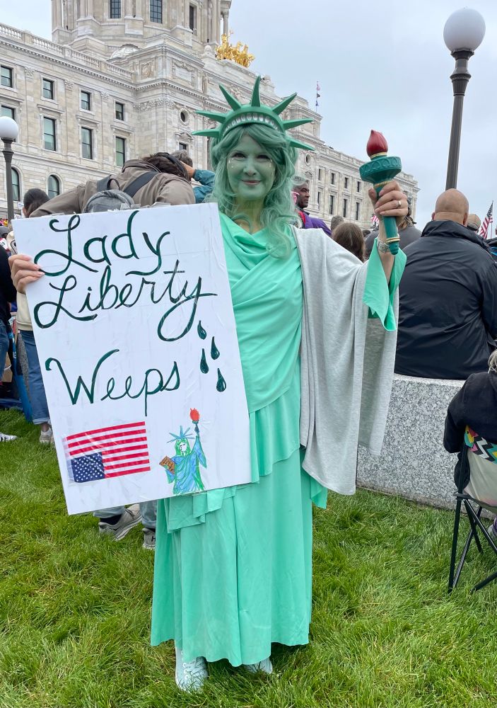 Woman dressed as Statue of Liberty with sign: “Lady Liberty weeps.”