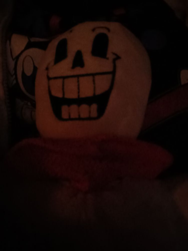 A Papyrus plush being held in a dark theatre by a weirdo wearing a The Amazing Digital Circus Caine Hot Topic T Shirt and a Gray hoodie with Stitch from Lilo and Stitch wearing a Santa Hat on it.