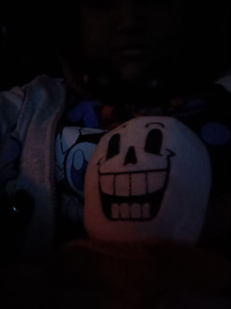 A Papyrus plush being held in a dark theatre by a weirdo wearing a The Amazing Digital Circus Caine Hot Topic T Shirt and a Gray hoodie with Stitch from Lilo and Stitch wearing a Santa Hat on it.