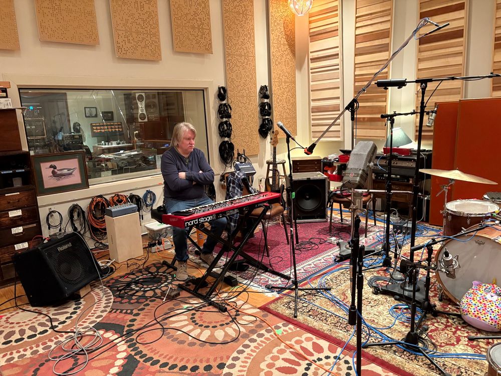 Scott Danbom sits in cross-armed judgement behind his Nord keyboard. Microphones, musical equipment and cables litter his domain.