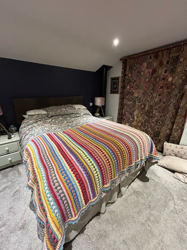 Cozy bed with beautiful, stripy blanket, crocheted in bright, cheerful colours.