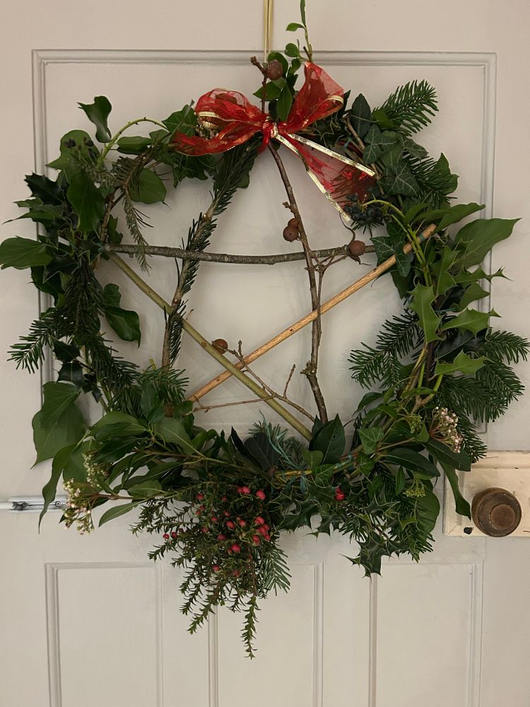 Christmas wreath with pentagram in the centre made from twigs from 5 different native trees.  Surrounded by evergreen foliage with berries and flowers. 