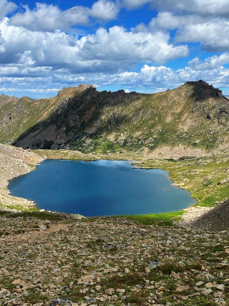 bright, deep blue lake surrounded by green meadows and rugged mountain peaks