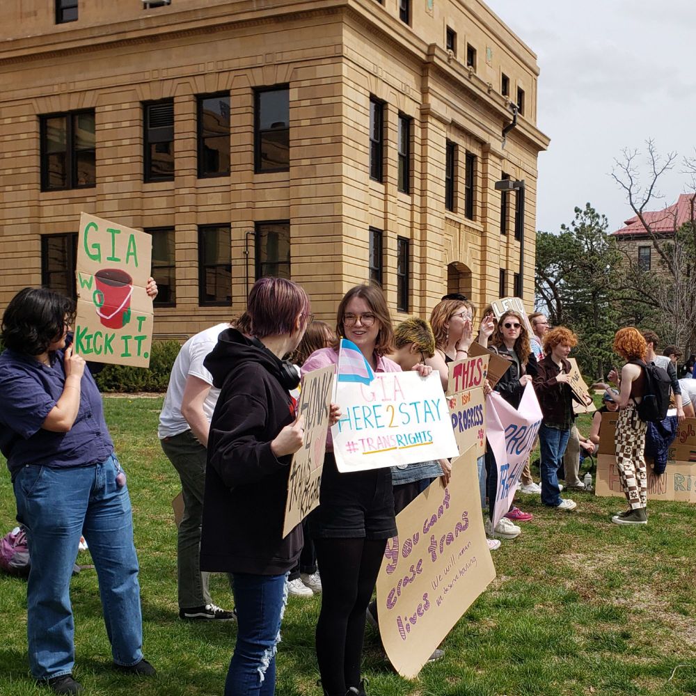 Student demonstrators in front of Strong Hall. Signs: GIA Here2Stay, #TransRights. You can't erase trans rights. GIA won't kick it (drawing of a bucket)