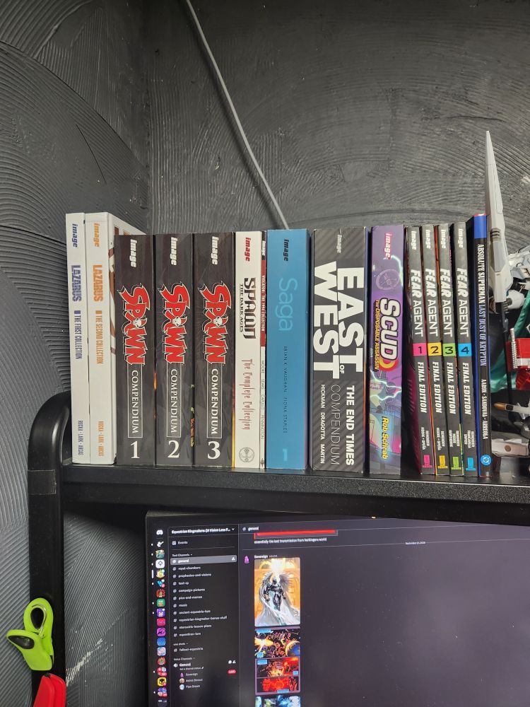 a small collection of image comics from left to right on screen it goes Lazurus, spawn, spawn medival dark ages and the violator mini series, saga, east of west, scud the disposable assassin and fear agent with. hardcover copy of absolute Superman at the end.