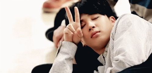 Sleepy Jimin cutely holding a peace sign against his face gif