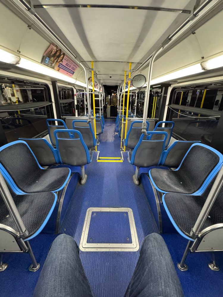 An empty Chicago bus except for the driver and a pair of legs in blue jeans. Every seat is empty. It is dark outside. It feels grandiose. 