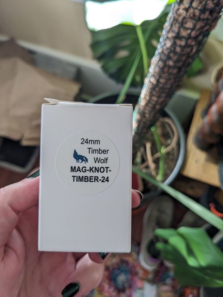 My big pale paw holding a box with a sticker that has an image of a howling wolf and reads "24mm Timber Wolf MAG KNOT TIMBER"