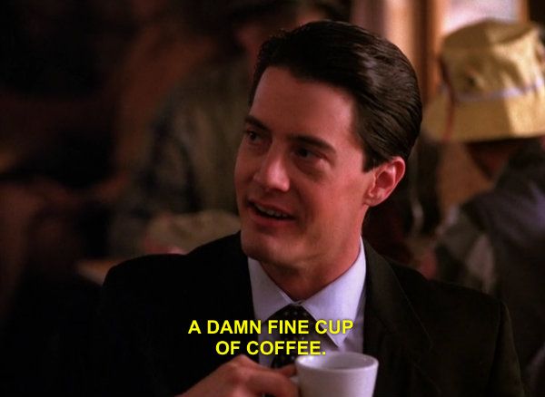 Dale Cooper from the TV show Twin Peaks, played by Kyle McLachlan a pale masculine fella in a standard suit that loudly reads him as a federal officer, holding a cup of coffee and the subtitles in yellow below show him as being caught saying "A Damn Fine cup of coffee!". His love, and addiction to coffee is a recurring theme in the show.