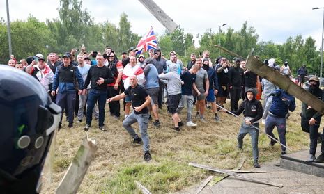 Photo from the summer 2024 UK far right riots. A group of men, gathered on a raised embankment, throwing projectiles at police. 