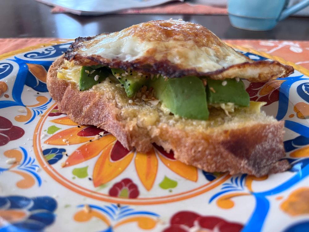 Sliced avocado and fried egg on top of a sourdough toast on a brightly colored plate