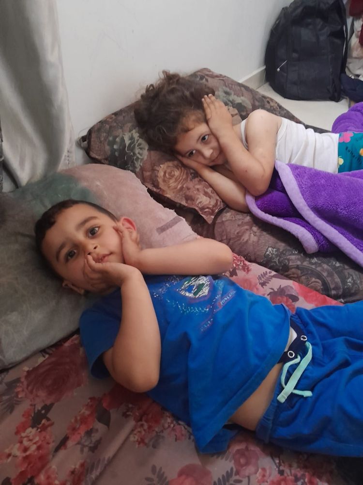 My friends Marwan and Dooa's small children lie on mats in their tent in Gaza, covering their ears/faces due to the sounds of drones and bombs. 