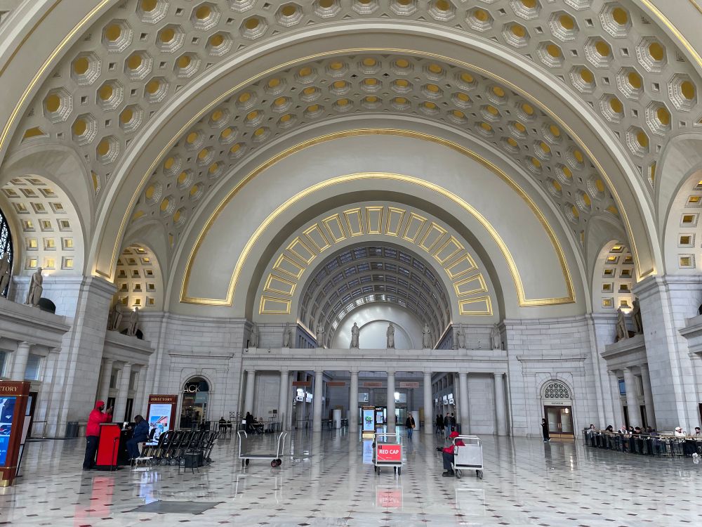 Photo of union station great hall (fairly empty) with a red cap sitting on a baggage cart 